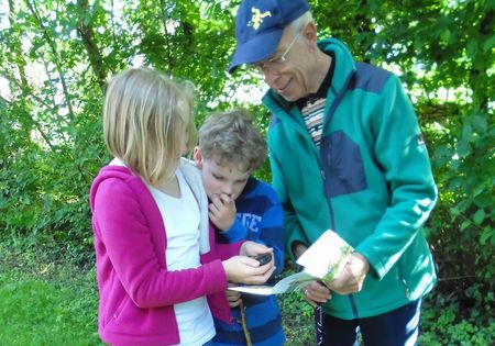 Kinder schauen sich das Tourenbuch für Kinder an mit grünen Bäumen im Hintergund